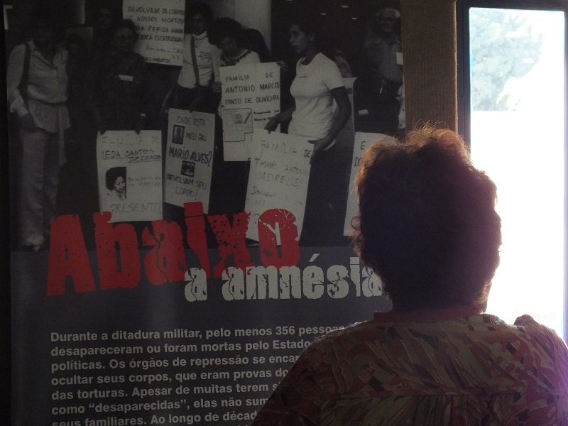 Amparo Almeida Araújo vor einem Plakat der Ausstelung "Amnestie und Demokratie" mit dem Spruch"Nieder mit der Amnestie" // C: Sara Fremberg